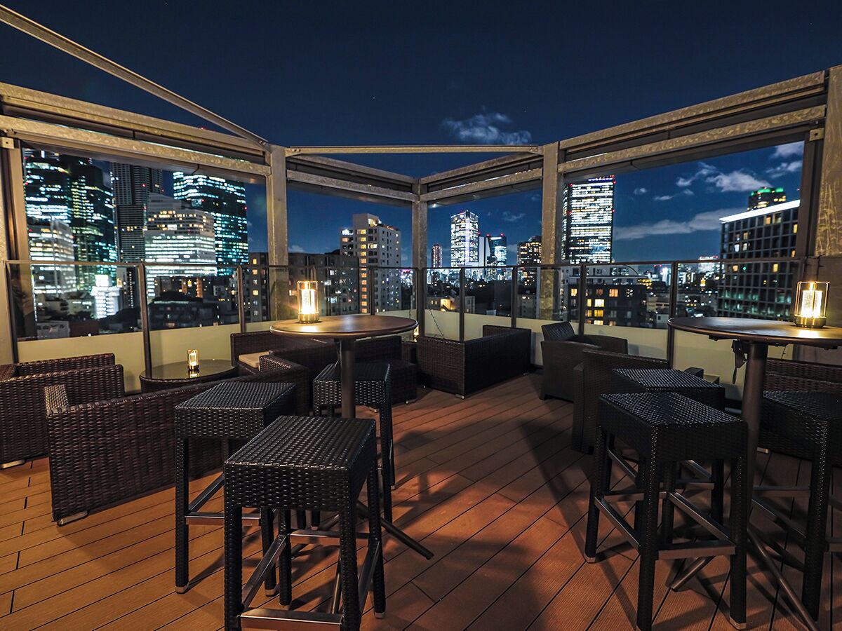 An outdoor seating area with tables and chairs, overlooking a cityscape at night.