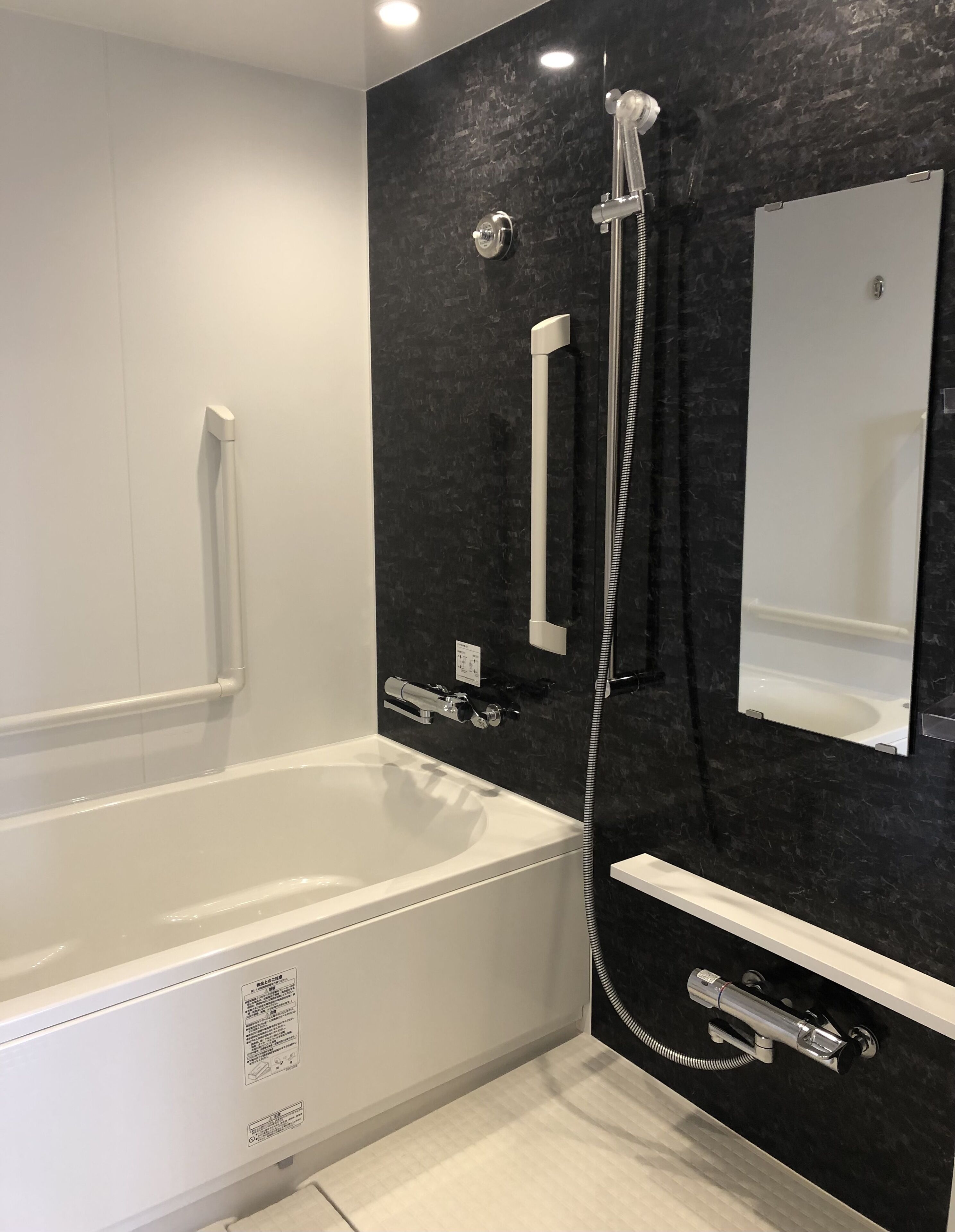 A modern bathroom with a white bathtub, a black marble wall, and a large mirror.