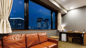 A hotel room with a leather sofa, a small desk, a refrigerator, and a view of city buildings at night. - HOTEL SUI AKASAKA byABEST (Tokyo)