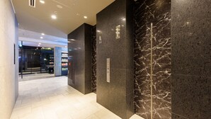 Un pasillo moderno con paredes de mármol oscuro y suelo de baldosas, que conduce a un acceso por puerta de vidrio.
