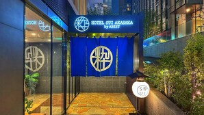 La entrada al Hotel Sui Akasaka de ABEST, con un diseño moderno que incluye un toldo azul y un camino empedrado que lleva a la entrada.