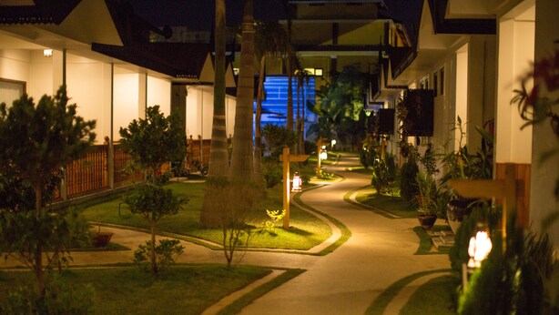 A nighttime view of a hotel corridor with illuminated pathways, palm trees, and a well-maintained lawn. - Spring Lodge Inle (Nyaungshwe)