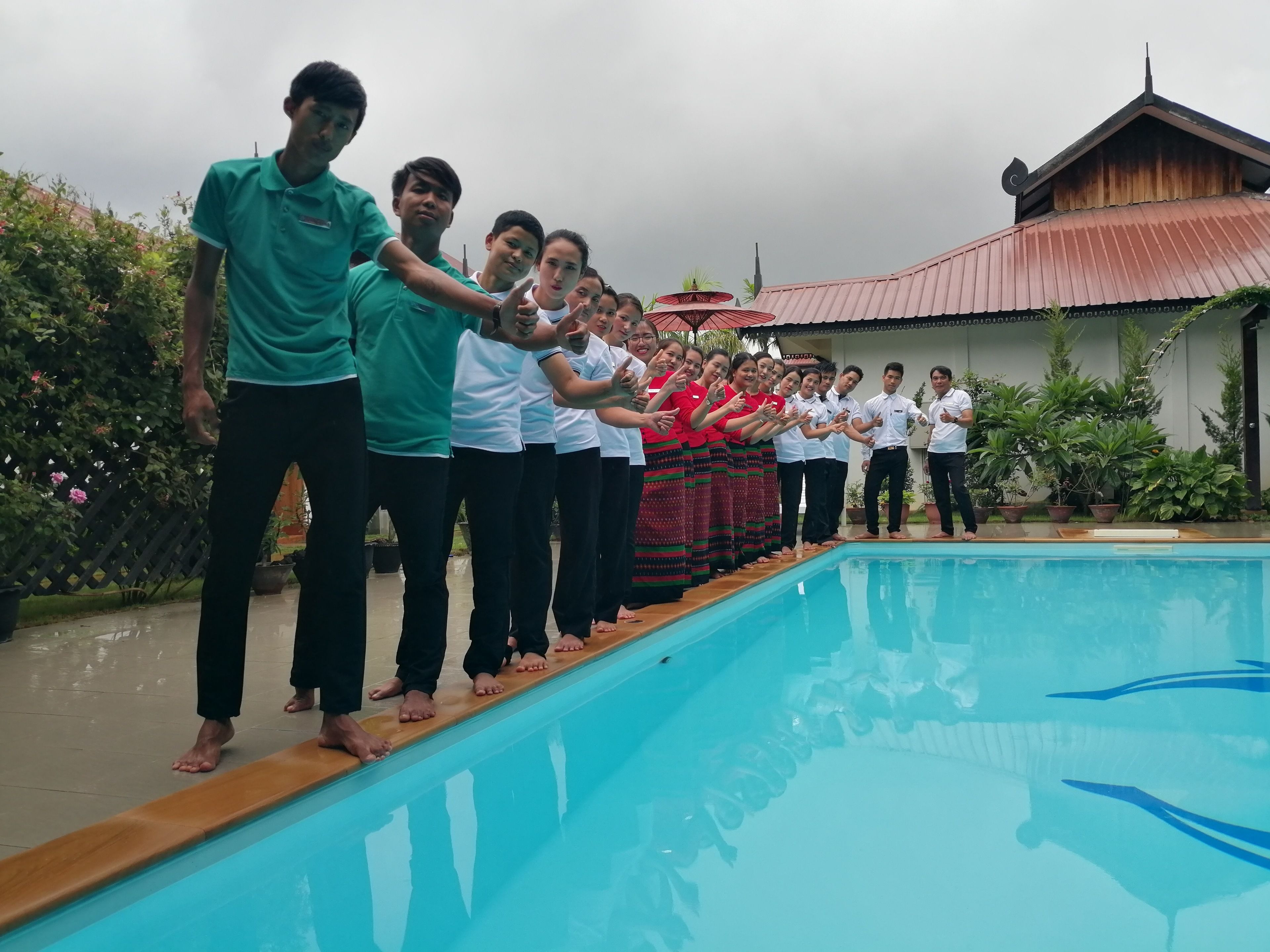 Un groupe de personnes se tient près d’une piscine, avec un bâtiment en arrière-plan.