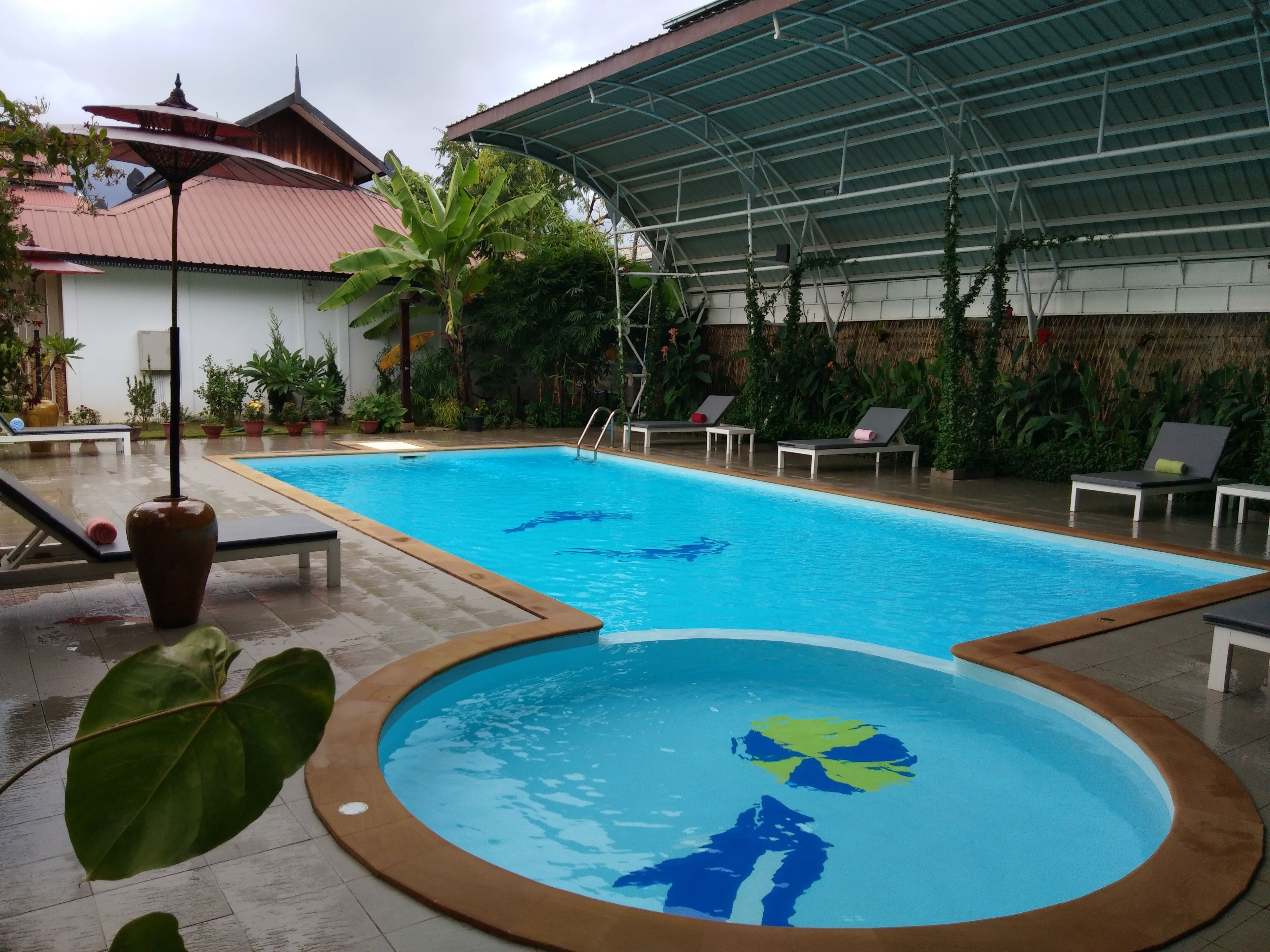 Ein Pool mit überdachtem Bereich, Liegestühlen und Topfpflanzen.