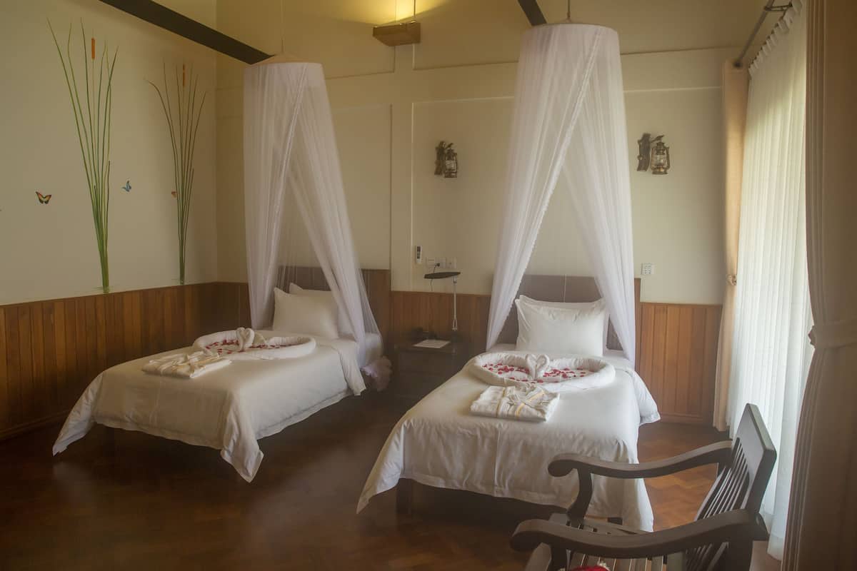 A room with two beds, each with a canopy, and a wooden bench.