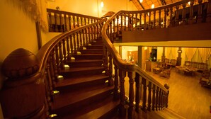 A grand staircase with wooden balusters leading to a second-floor area with seating and a fireplace. - Spring Lodge Inle (Nyaungshwe)