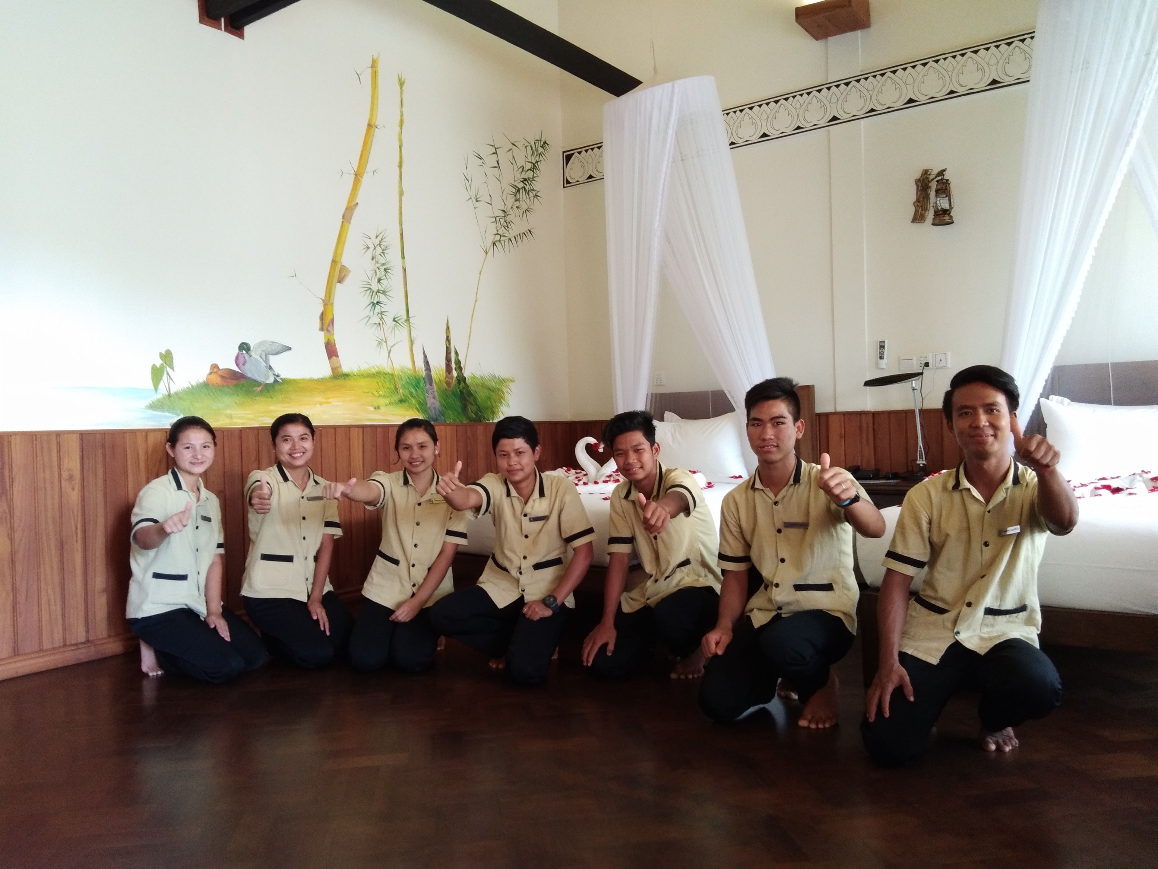 Un grup de persones en una habitació amb un mural de bambú i un llit amb roba de llit blanca.