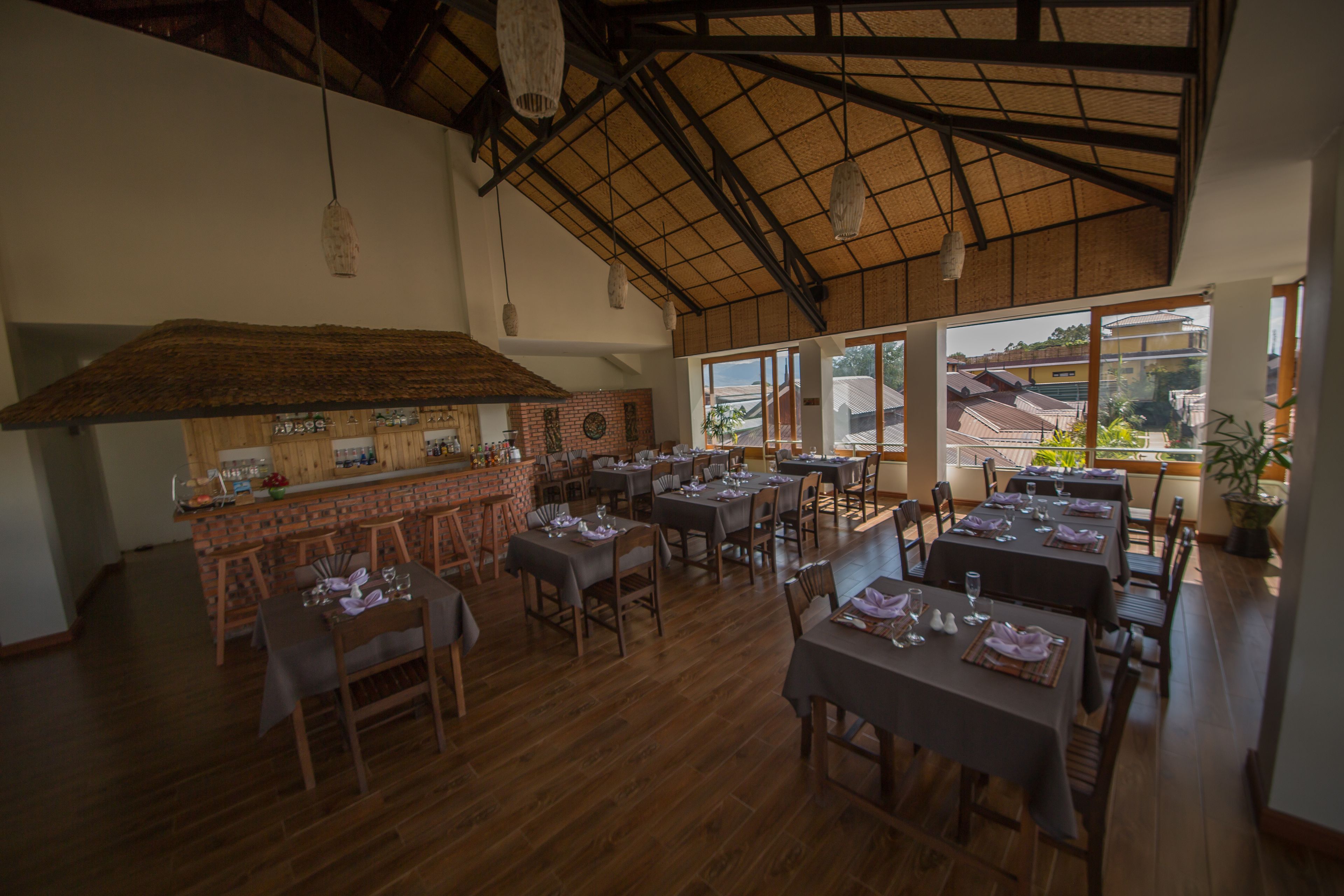 Un restaurante con mesas y sillas de madera, una zona de bar y amplios ventanales que ofrecen vistas al exterior.