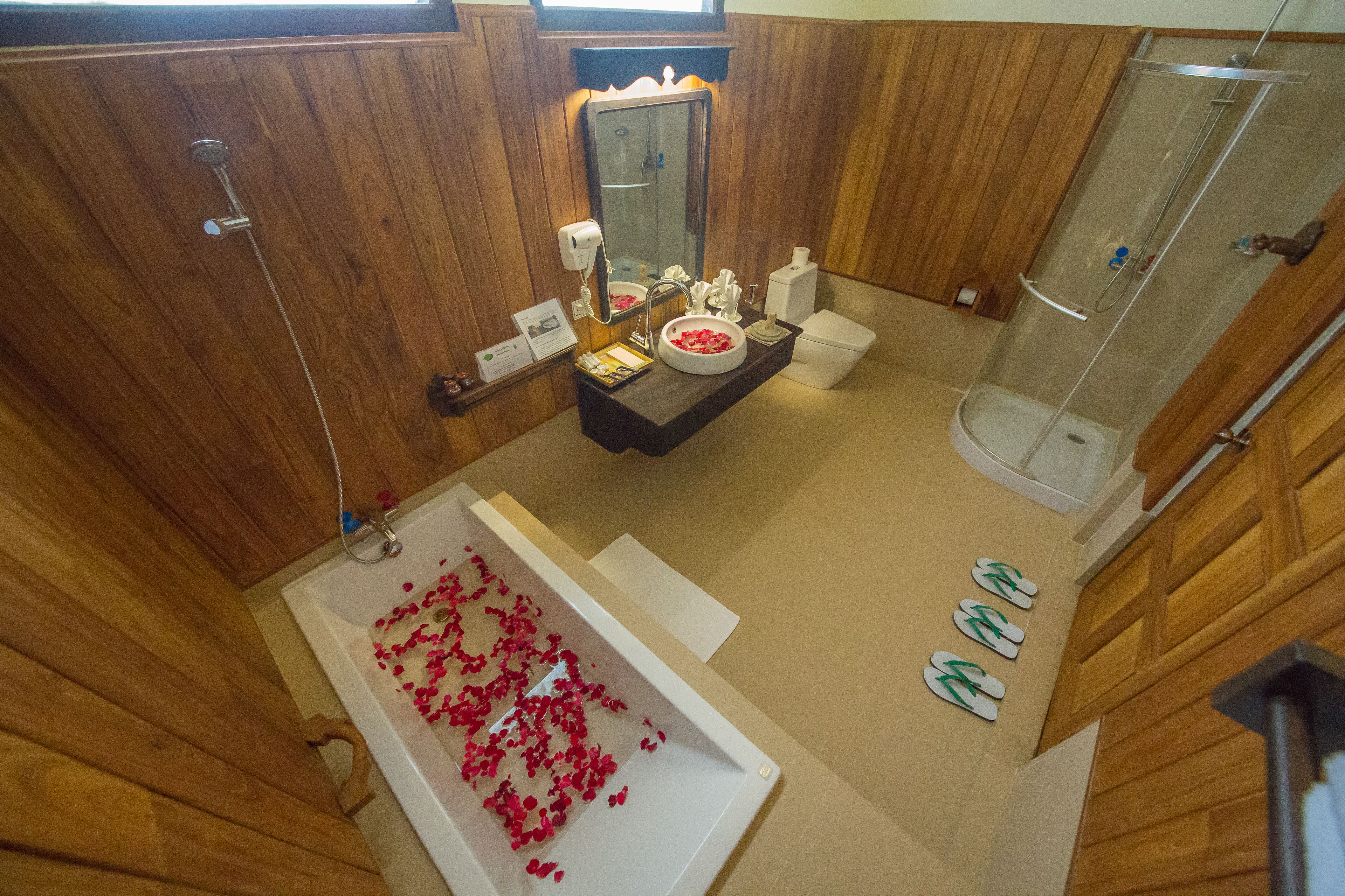 Een badkamer met houten inrichting, een bad met rozenblaadjes, een douche en een toilet.