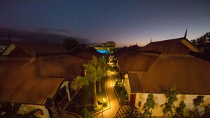 A nighttime view of a resort with a central pathway, palm trees, and buildings with thatched roofs. - Spring Lodge Inle (Nyaungshwe)