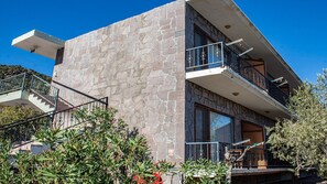 A modern two-story building with a stone facade, a balcony with metal railings, and a staircase leading to the entrance. - Sivrice Sarnıç (Ayvacik)