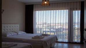 A hotel room with a large bed, a smaller bed, a view through sheer curtains, and a hanging light fixture. - Sivrice Sarnıç (Ayvacik)