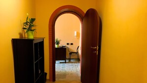 A hallway with a tiled floor, a wooden door, a potted plant, and a desk with a chair. - Residenza Viviani (Sant'Agnello)