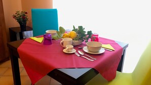 A dining table set with a red tablecloth, white bowls, cups, a basket of fruit, and a potted plant. - Residenza Viviani (Sant'Agnello)