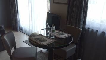 Un coin repas avec une table en verre, quatre chaises, deux bouteilles d’eau et un tableau encadré au mur.