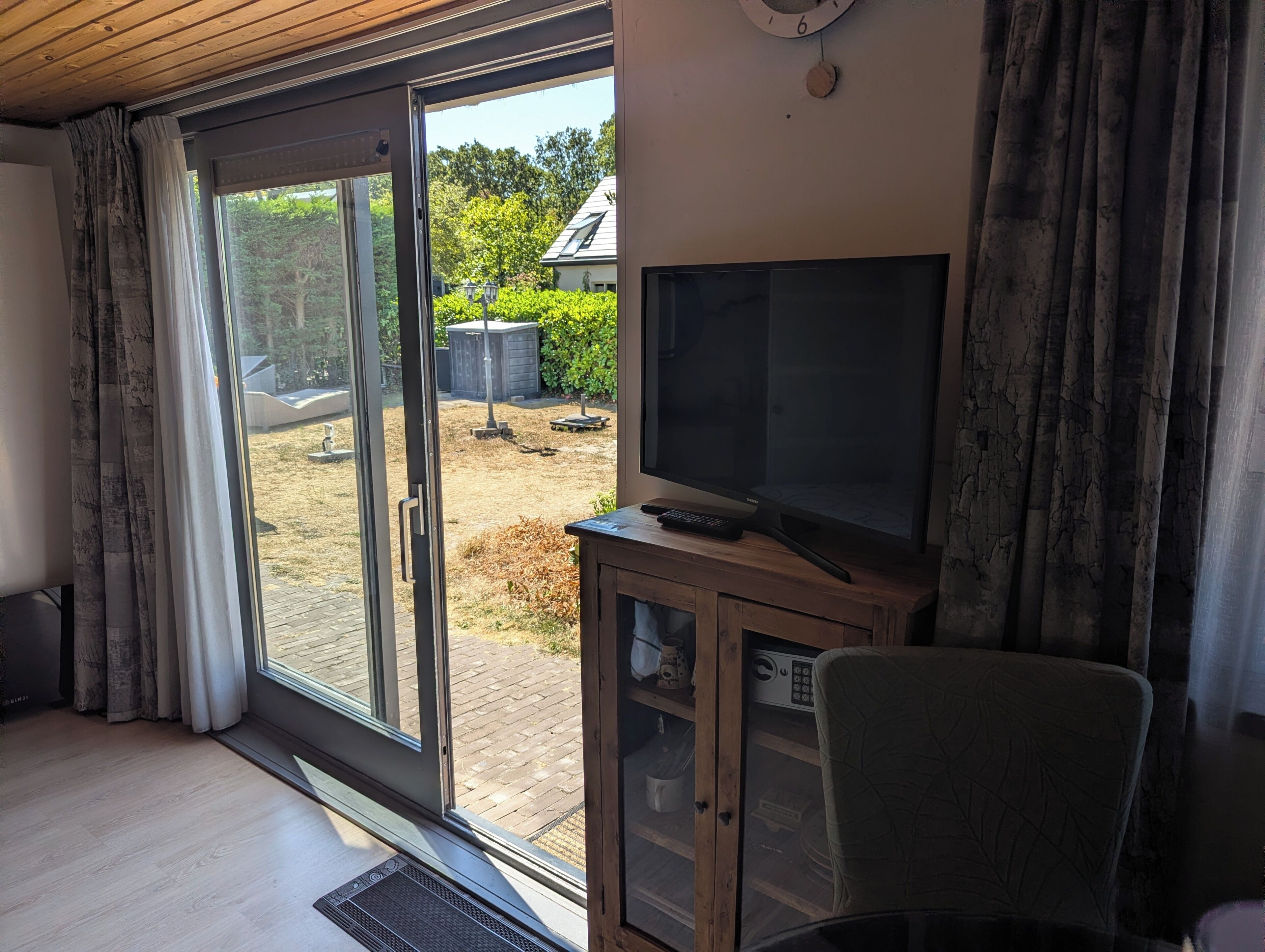 A room with a sliding glass door leading to a backyard, a television on a wooden cabinet, and a chair.