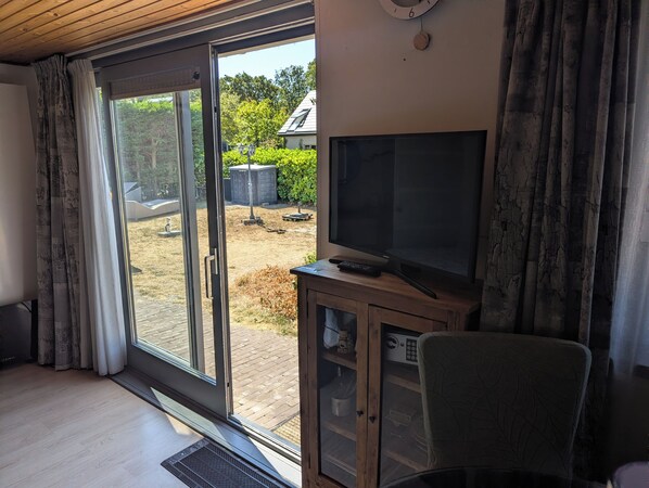 Una habitación con puerta corrediza de vidrio que da a un patio trasero, un televisor sobre un mueble de madera y una silla.