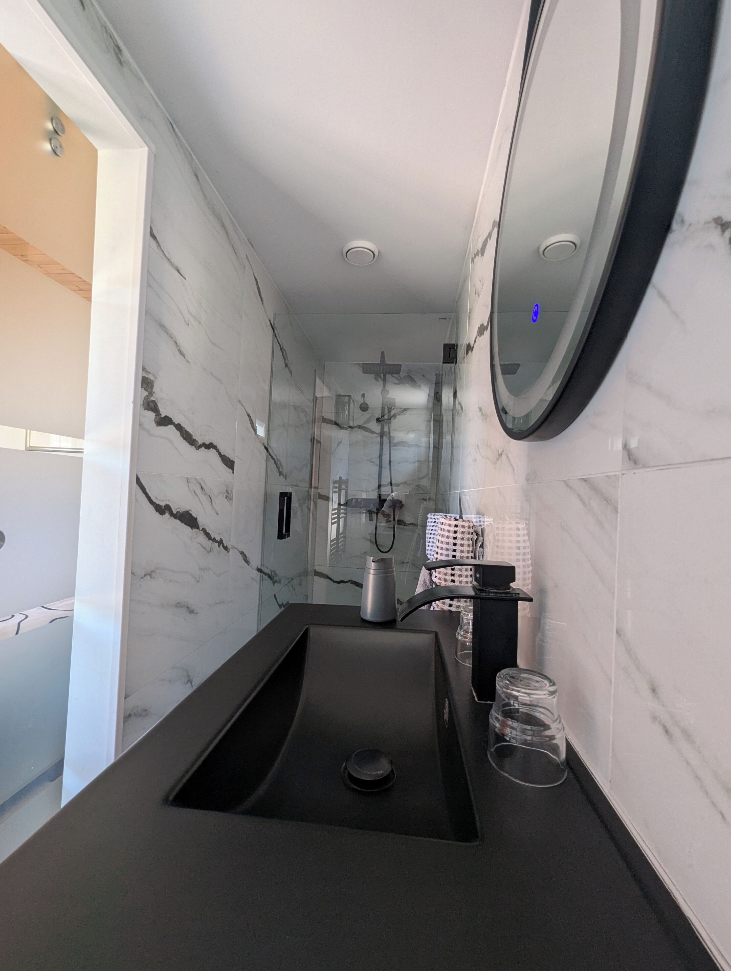 Un baño moderno con pared de mármol, un lavabo negro y cabina de ducha de vidrio.