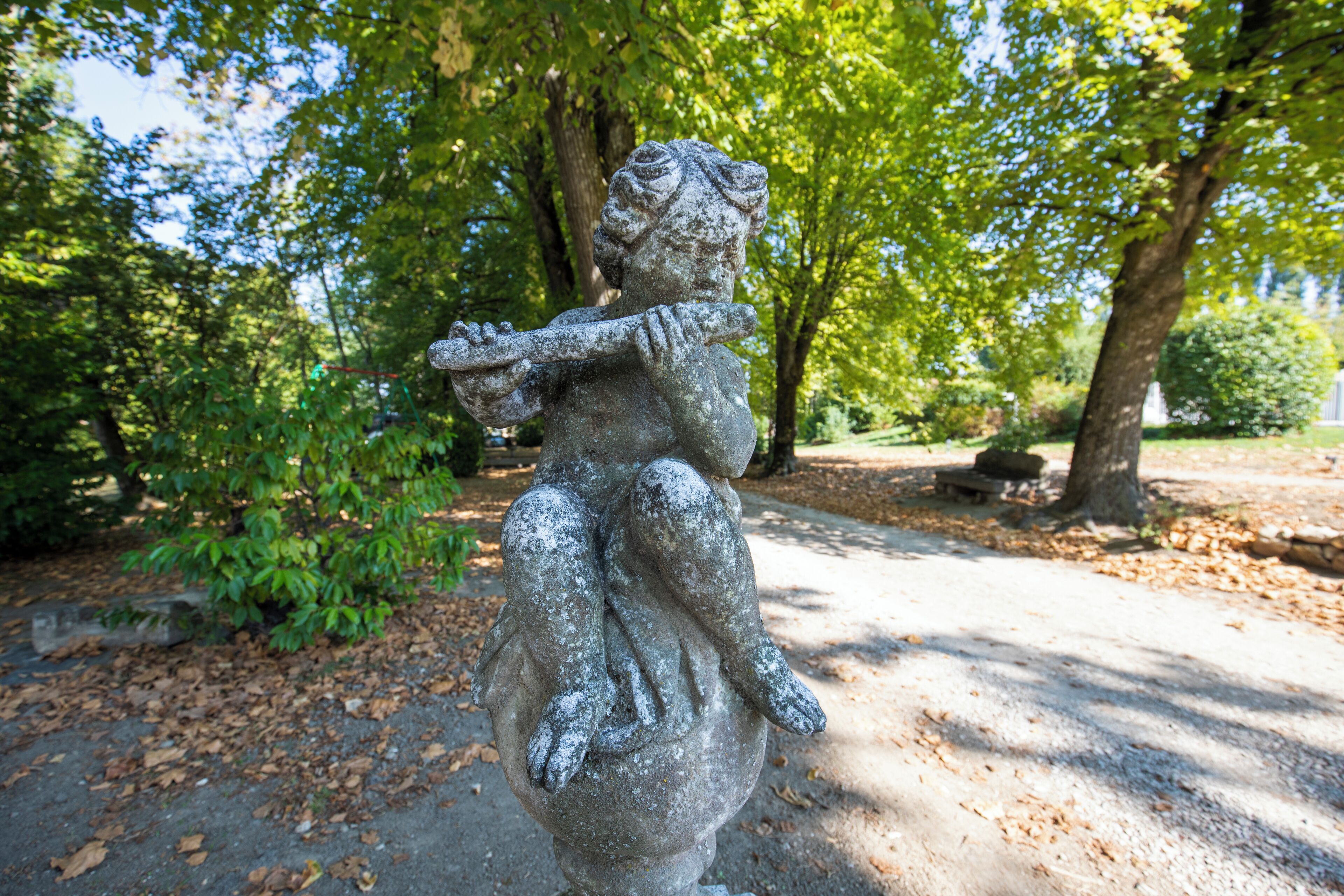 Eine Steinstatue einer Figur, die ein Kind in einer Parkanlage hält.