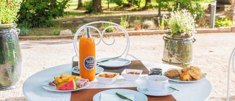 A round table with a white metal frame, set with plates of food, a bottle of orange juice, and a cup of coffee.