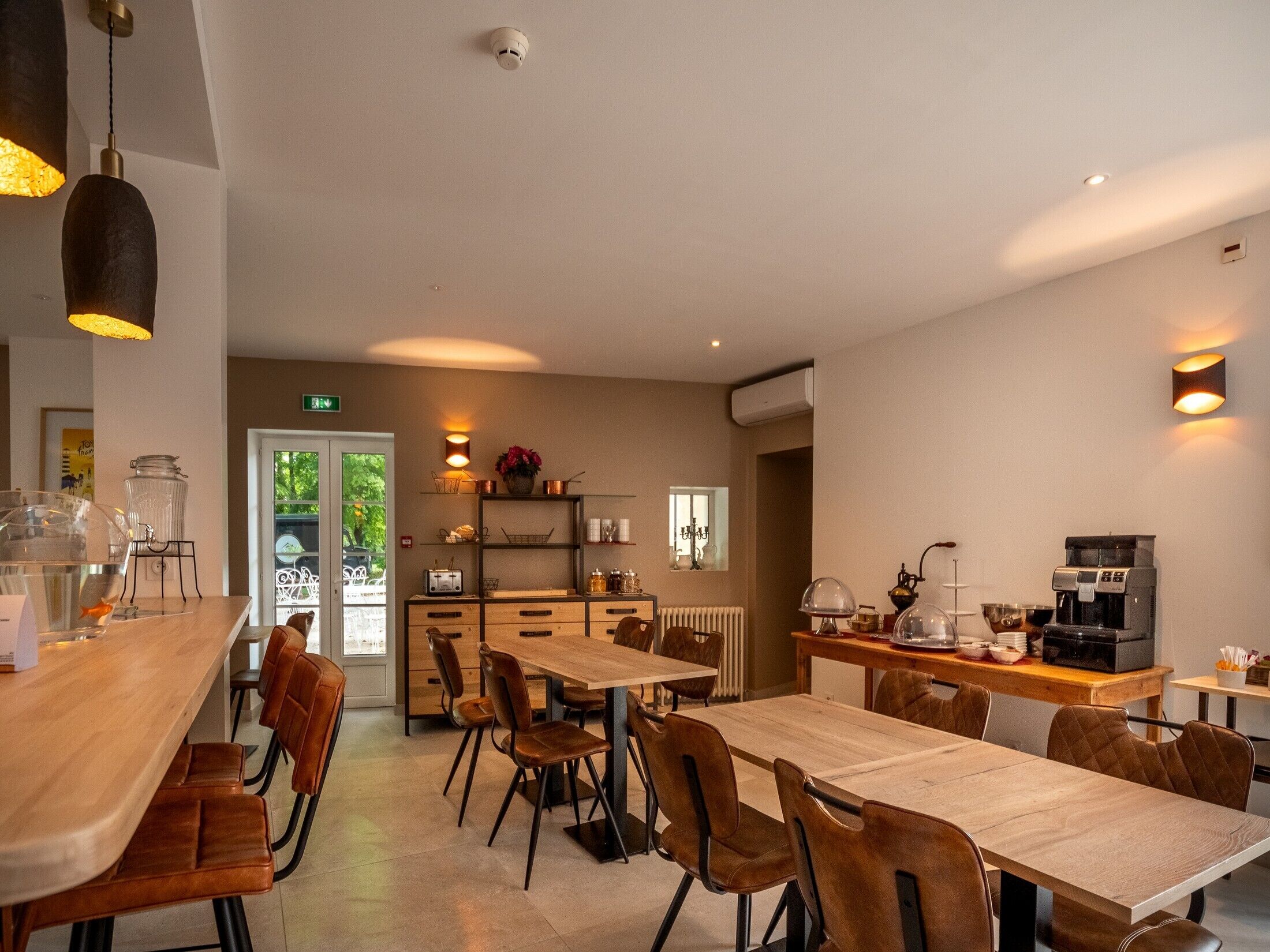 Un moderno comedor con mesas y sillas de madera, una máquina de café y un mostrador de buffet con diversas opciones de comida.