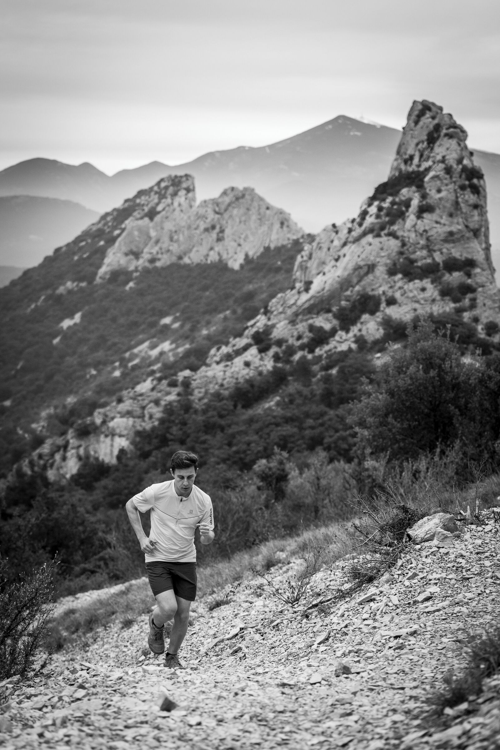 A person running on a rocky trail with mountains in the background.