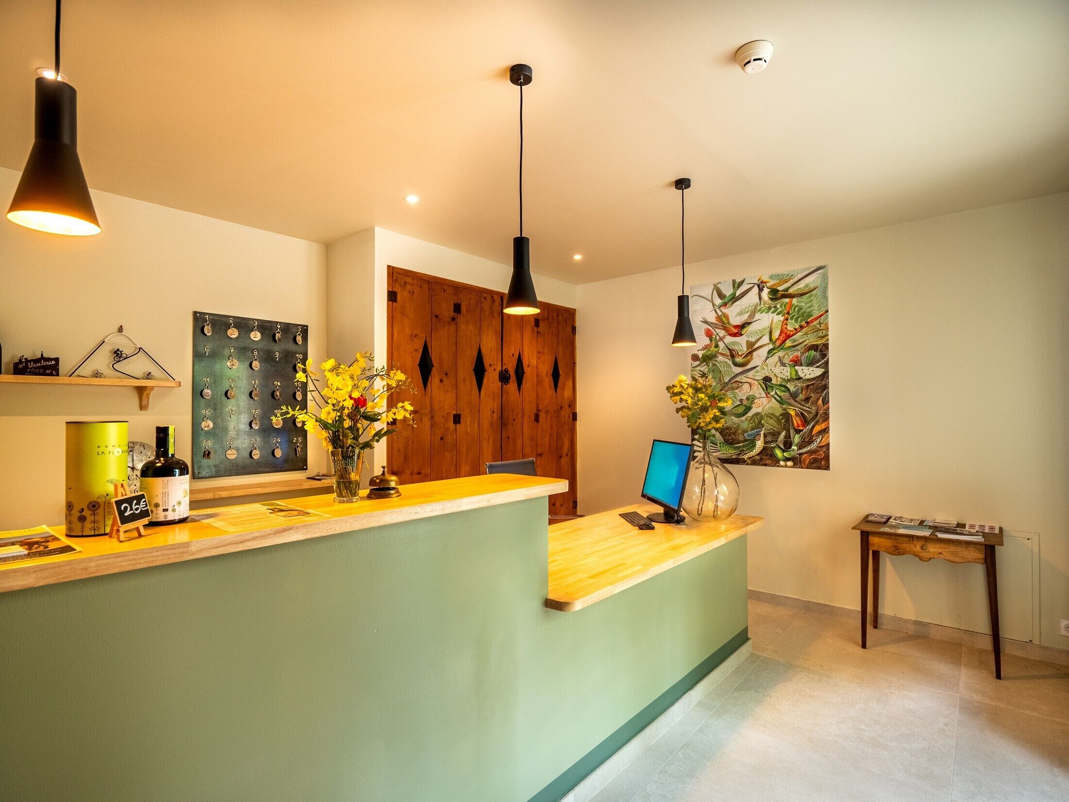 Een receptie met een houten balie, hanglampen, een computer en een wanddecoratie van een vogel.
