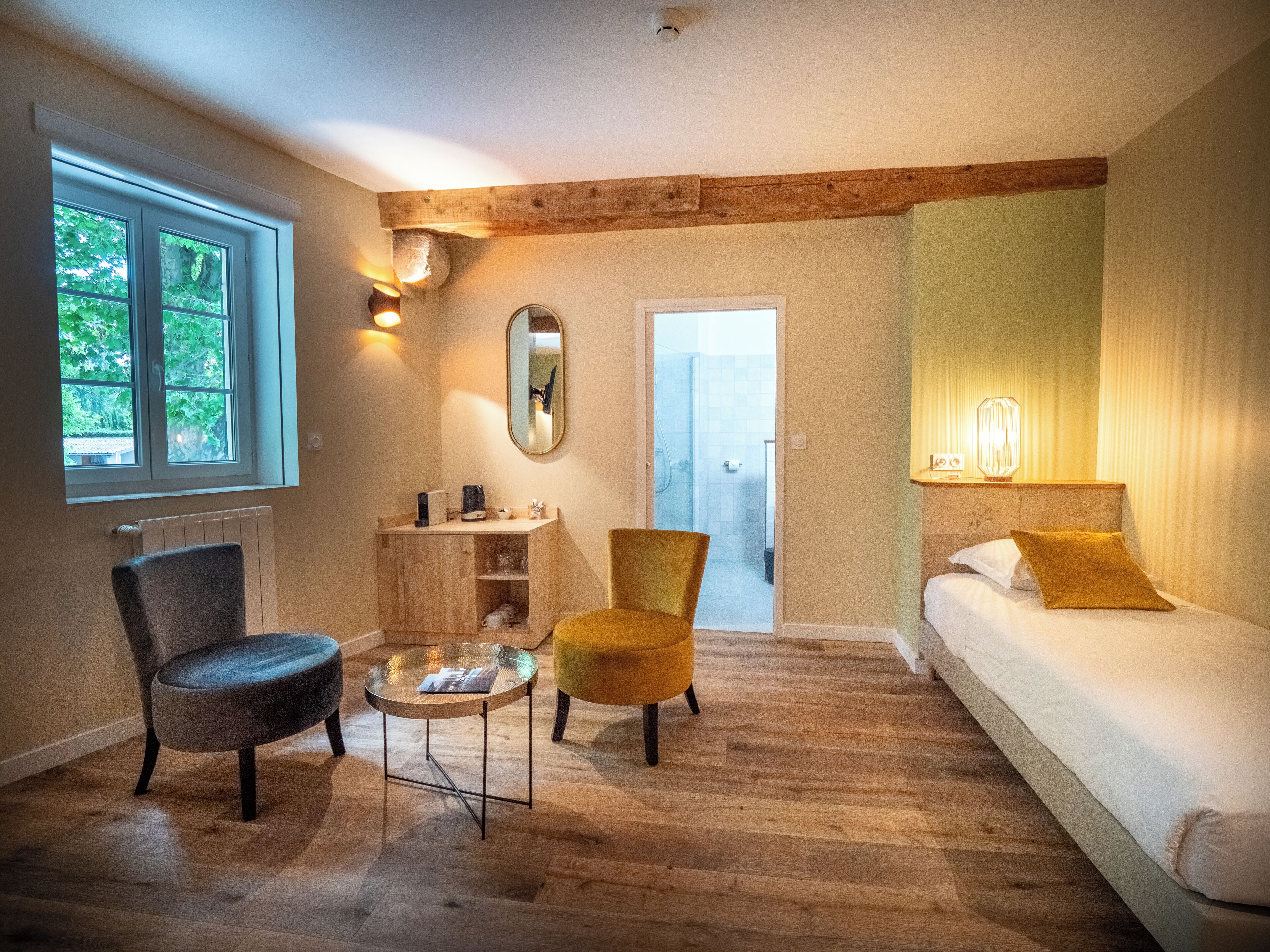 A room with a bed, two chairs, a small table, a mirror, and a window.