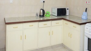 A kitchen with beige tiled walls, a microwave, a kettle, and a coffee maker on the counter. - Cozy and Furnished 1 Bedroom Apartment (Nairobi)