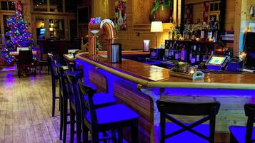 A bar area with wooden bar stools, a Christmas tree, and a variety of bottles on shelves.