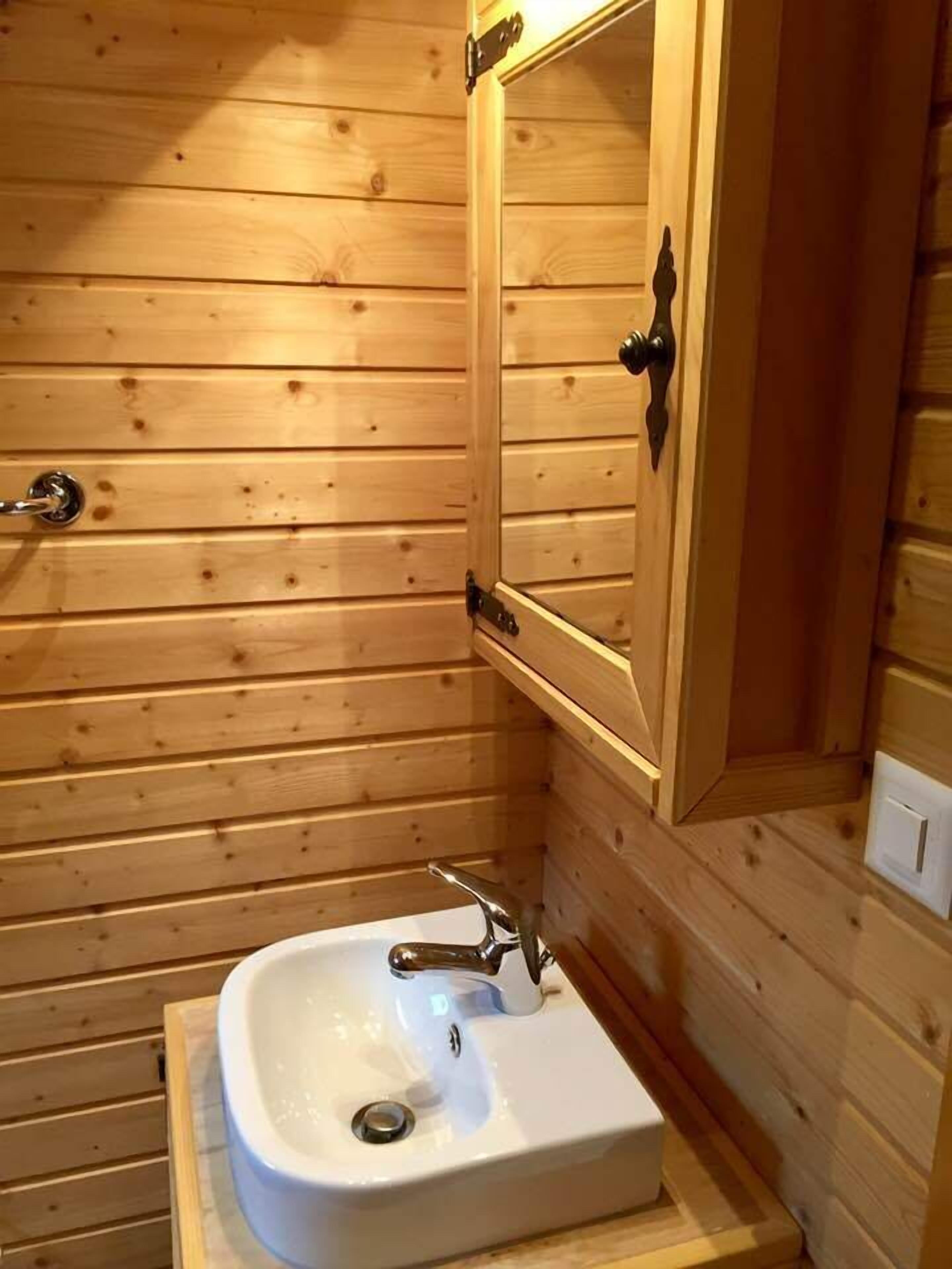 A wooden cabin bathroom with a white sink, wooden walls, and a mirror cabinet.