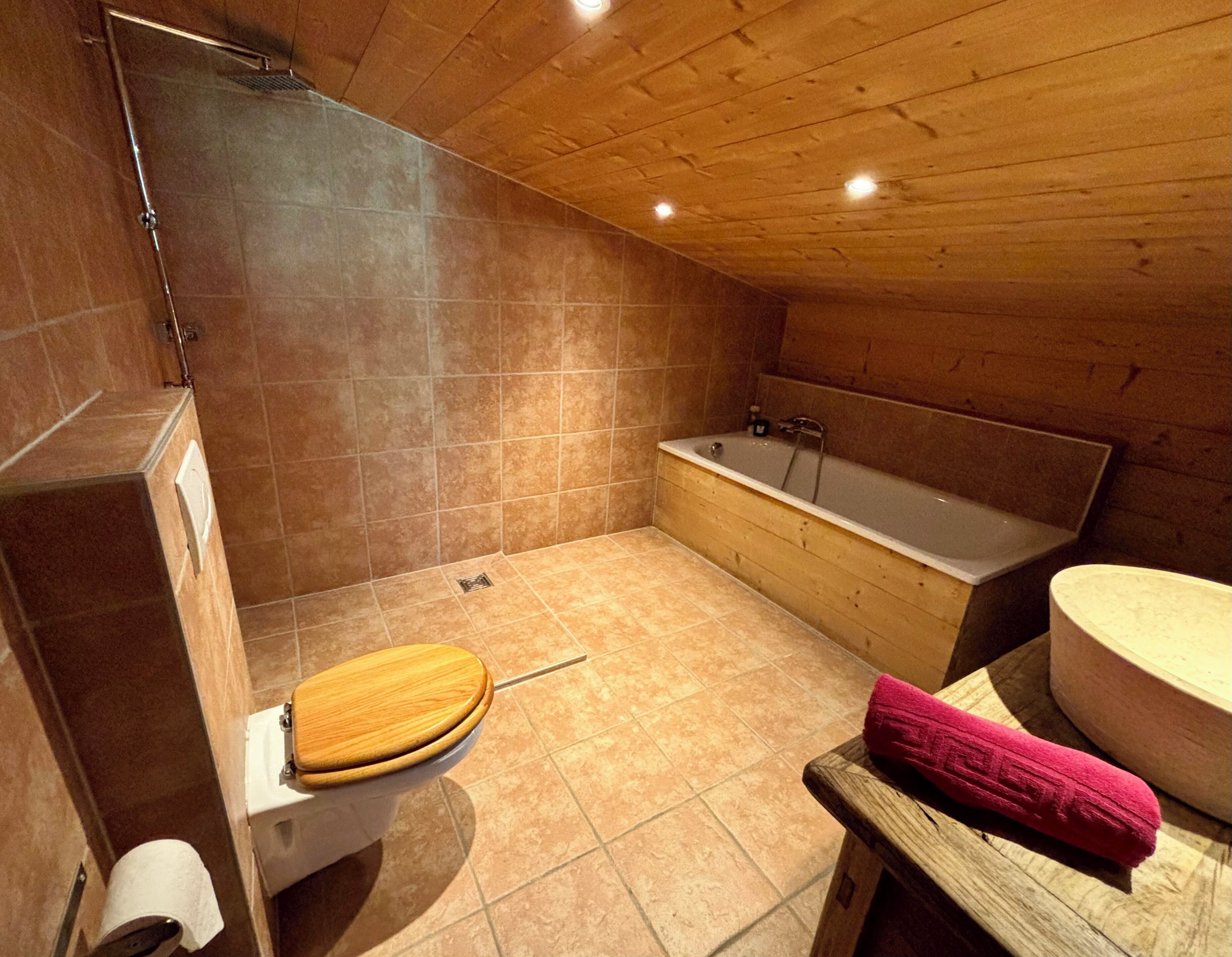 Une salle de bain avec un plafond en bois, une baignoire, des toilettes avec un abattant en bois et une douche.