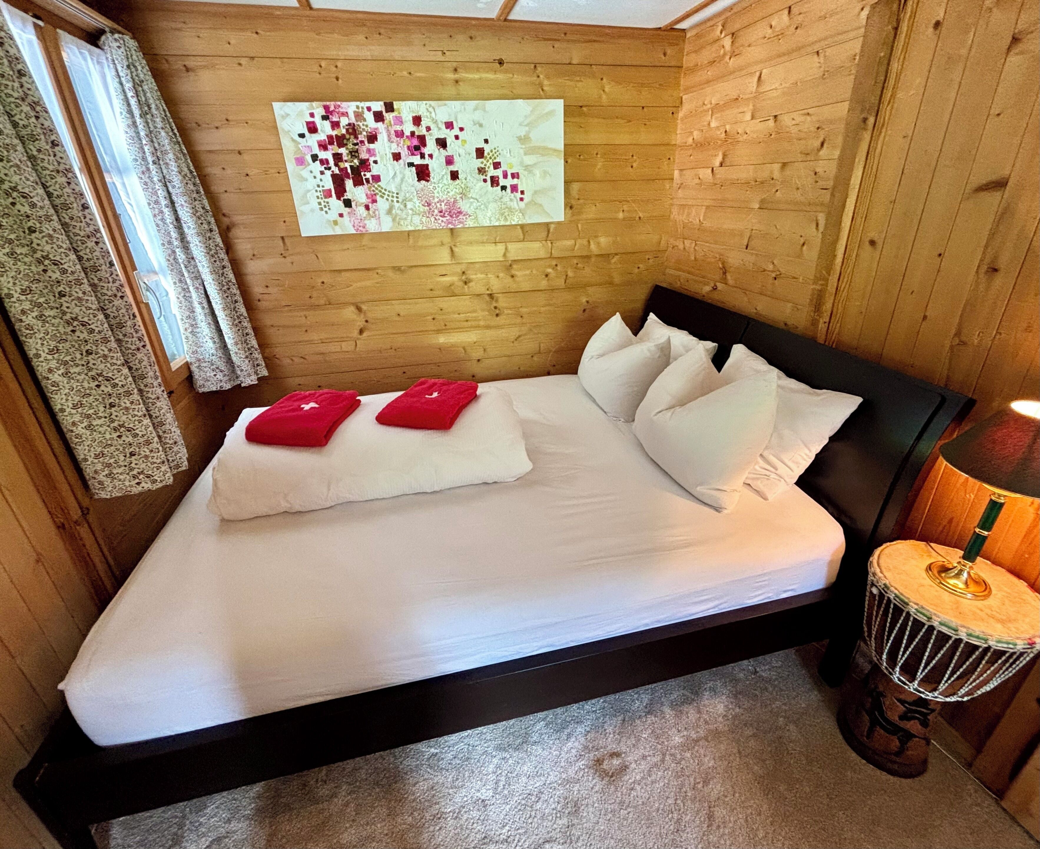 A wooden-paneled room with a bed, pillows, a wall hanging, and a drum.