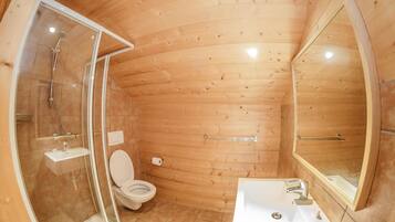 Een badkamer met houten lambrisering, een douchecabine met glazen wanden, een witte wastafel en een toilet.