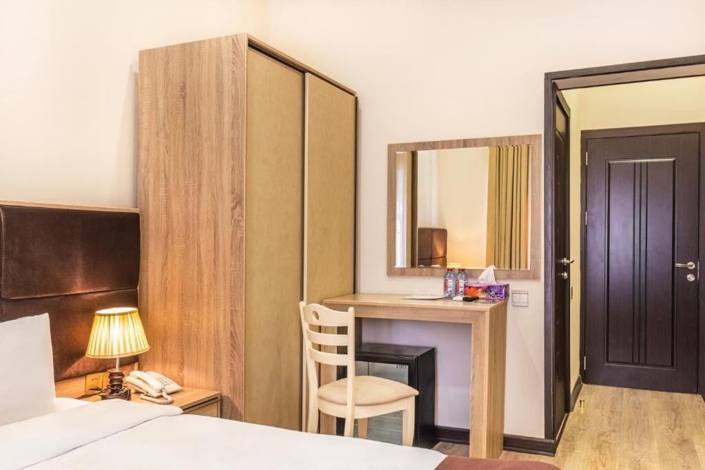 Habitación de hotel con cama, escritorio con silla, teléfono, espejo y armario.
