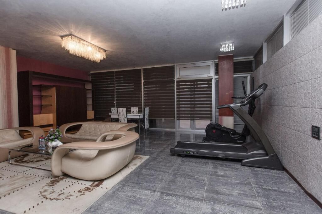 Uma sala de estar moderna com esteira, sofás de couro e uma janela grande com persianas.