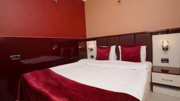A hotel room with a large bed, two nightstands, and a red wall.