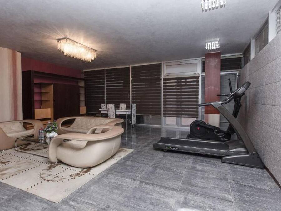 A modern living room with a sofa, a coffee table, a treadmill, and a large window with blinds.