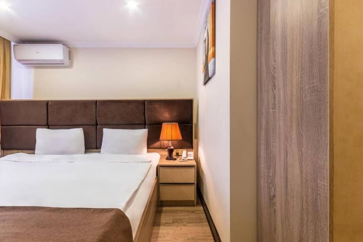 Una camera d'albergo con un letto grande, un comodino con una lampada e un condizionatore d'aria a parete.