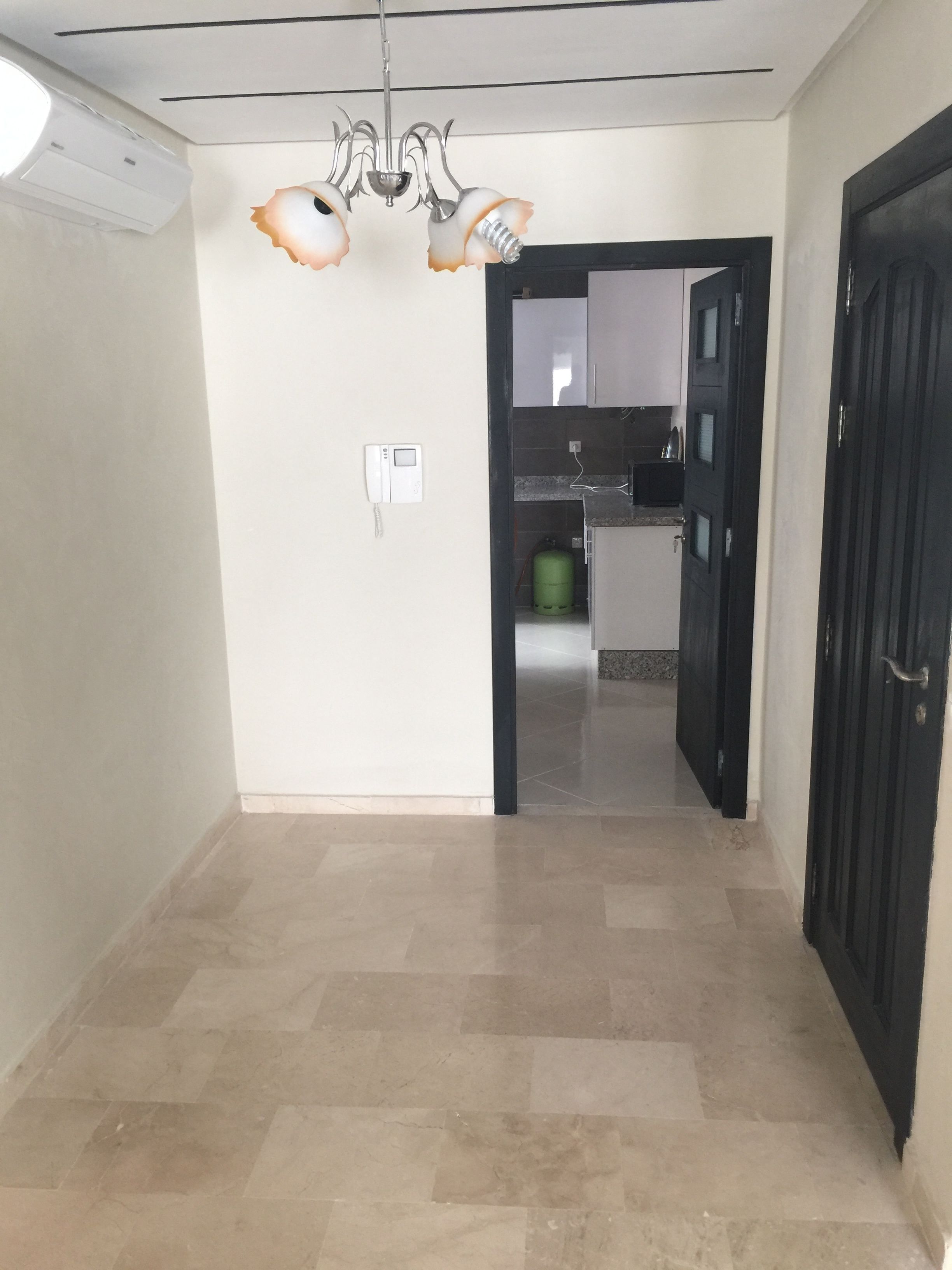 A hallway with a chandelier, a door, and a view into a kitchen area.