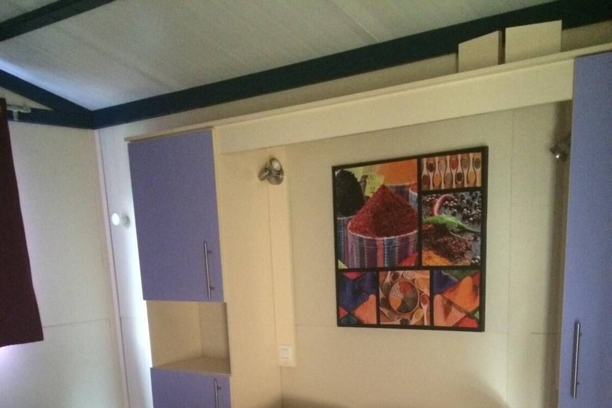 A single-bed room with a striped mattress, a pillow, a folded blanket, and a wall-mounted shelf.