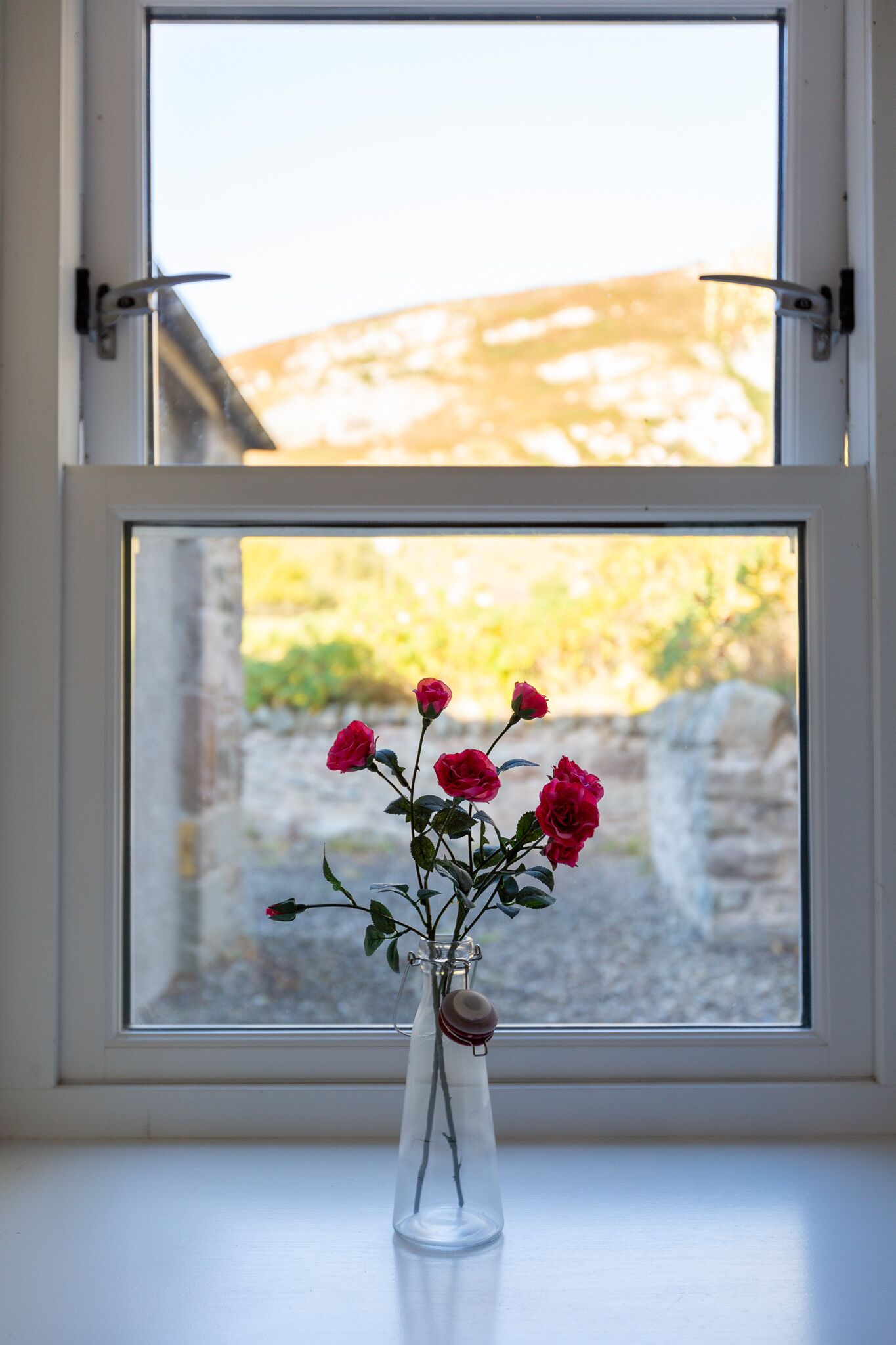 A clear glass vase with roses on a windowsill.