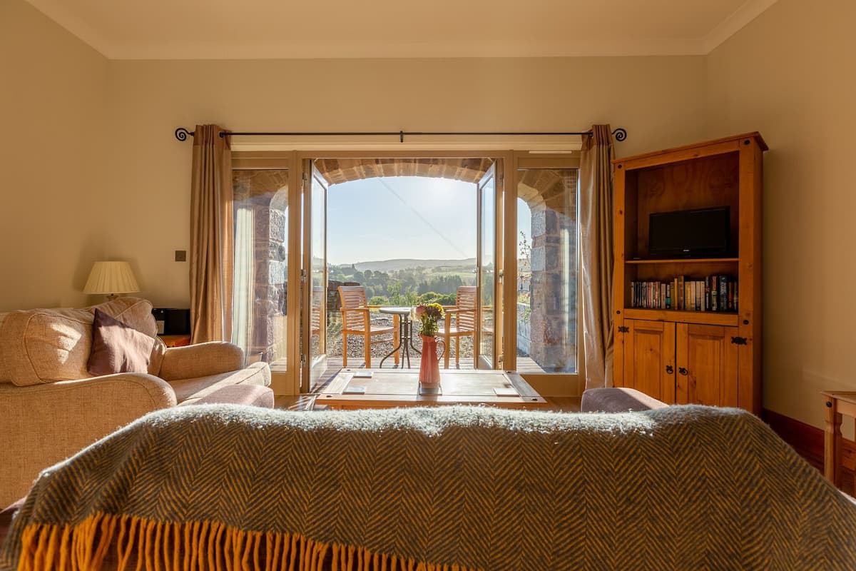 Quarto com uma grande janela, um sofá, um móvel para televisão e vista para o campo.
