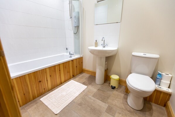A bathroom with a wooden floor, white tiles, a bathtub, a sink, and a toilet. - Kennacoil (Dunkeld)