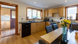 A modern kitchen with wooden cabinets, a built-in microwave, and a dining area with a table and chairs. - Kennacoil (Dunkeld)