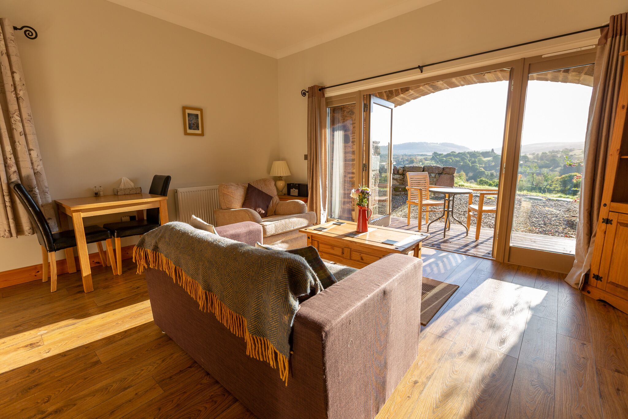 Una sala de estar acogedora con un sofá, una mesa de centro y un comedor con sillas y una mesa. Hay un ventanal con vistas al exterior.