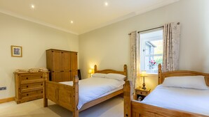 A bedroom with two wooden beds, a wooden wardrobe, a bedside table with a lamp, and a window with curtains. - Kennacoil (Dunkeld)