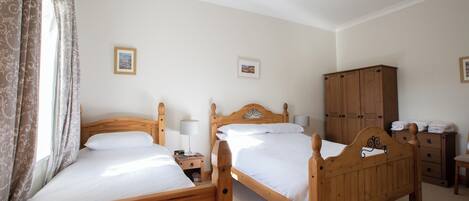 A bedroom with two wooden beds, a wardrobe, and a small bedside table with a lamp.