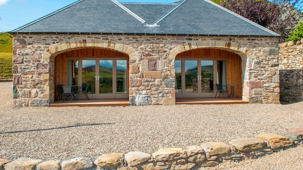 A stone building with two large arched windows and a gravel driveway. - Kennacoil (Dunkeld)
