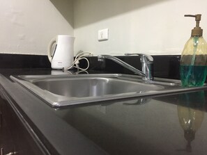 A kitchen with a stainless steel sink, a coffee maker, and a bottle of hand soap.